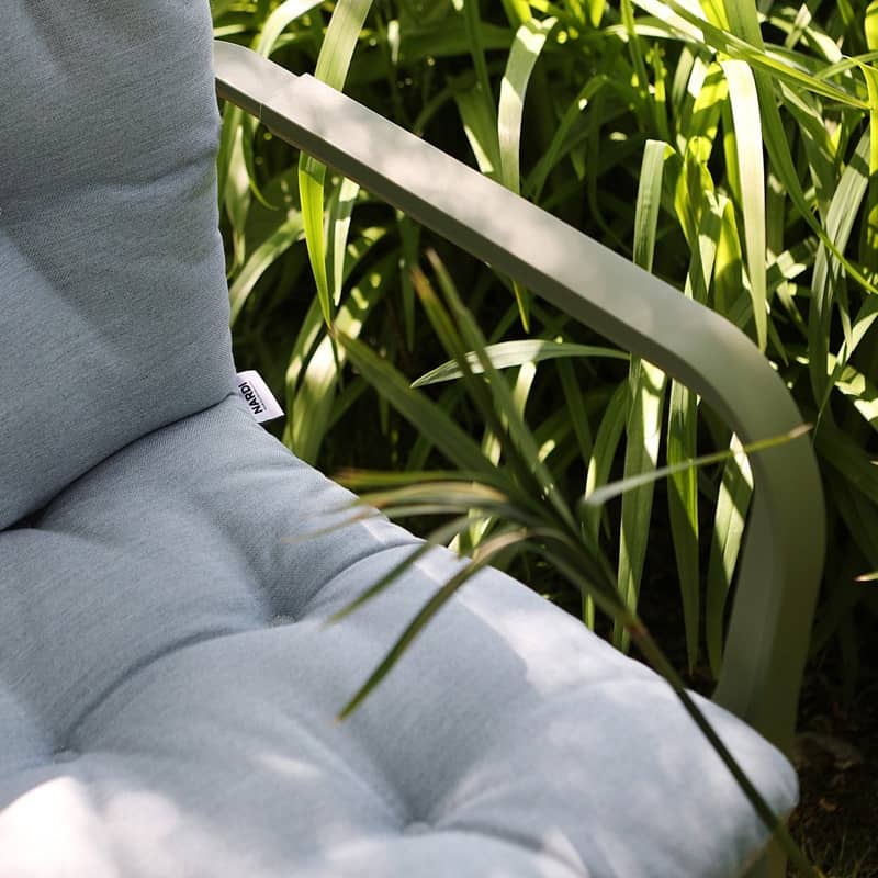 Detailansicht eines gepolsterten Stuhls, der draussen bei Sonnenschein im hohen Gras steht